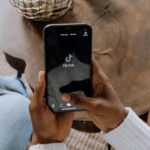 Close-up of hands holding a smartphone displaying the TikTok app interface on a wooden surface.