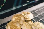 Close-up of gold Bitcoin coins on a laptop keyboard with a stock chart, symbolizing cryptocurrency market analysis.